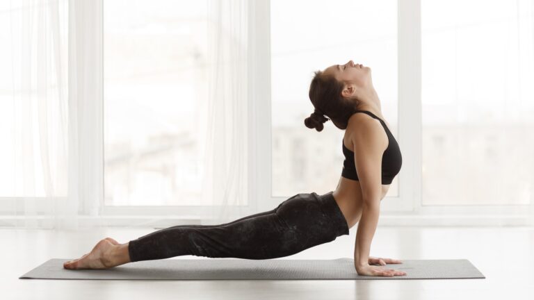 Fit woman making cobra pose on yoga mat