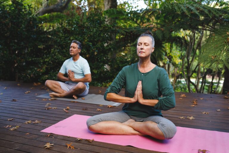 Happy senior caucasian couple practicing yoga, meditating in sunny garden